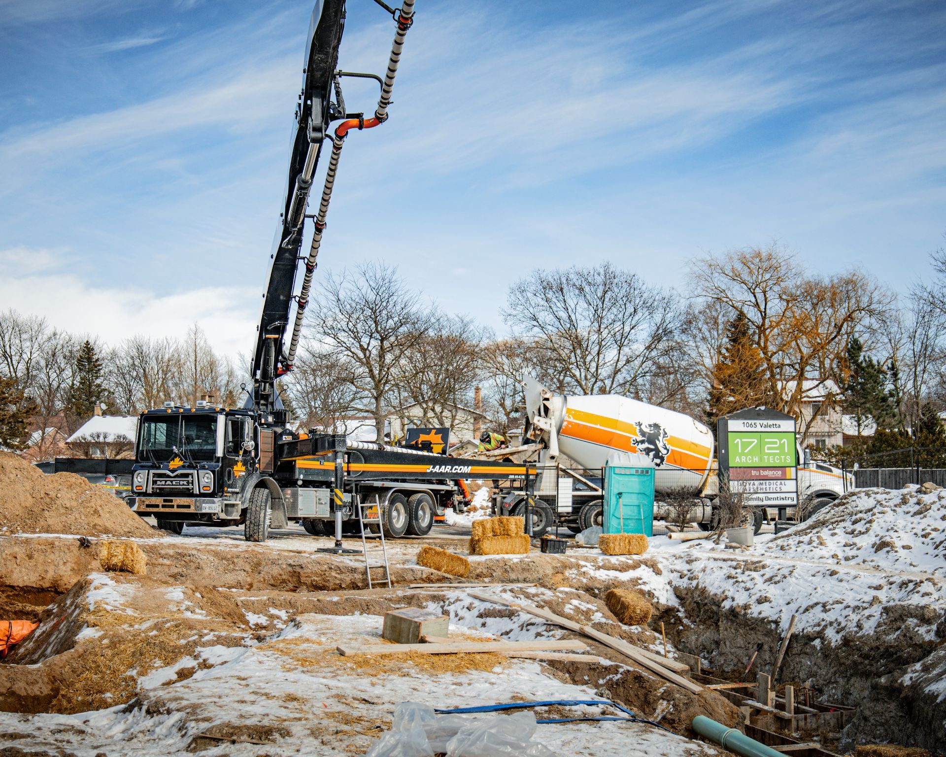 Construction site: concrete pump truck pouring concrete into a foundation. Snowy ground, bright sky.