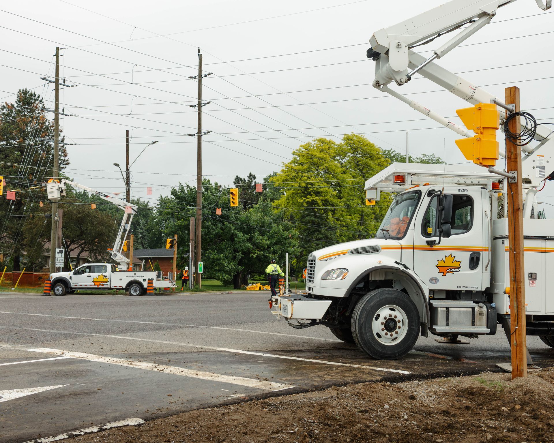 Two white utility trucks at an intersection; one with lift extended. Power lines overhead.