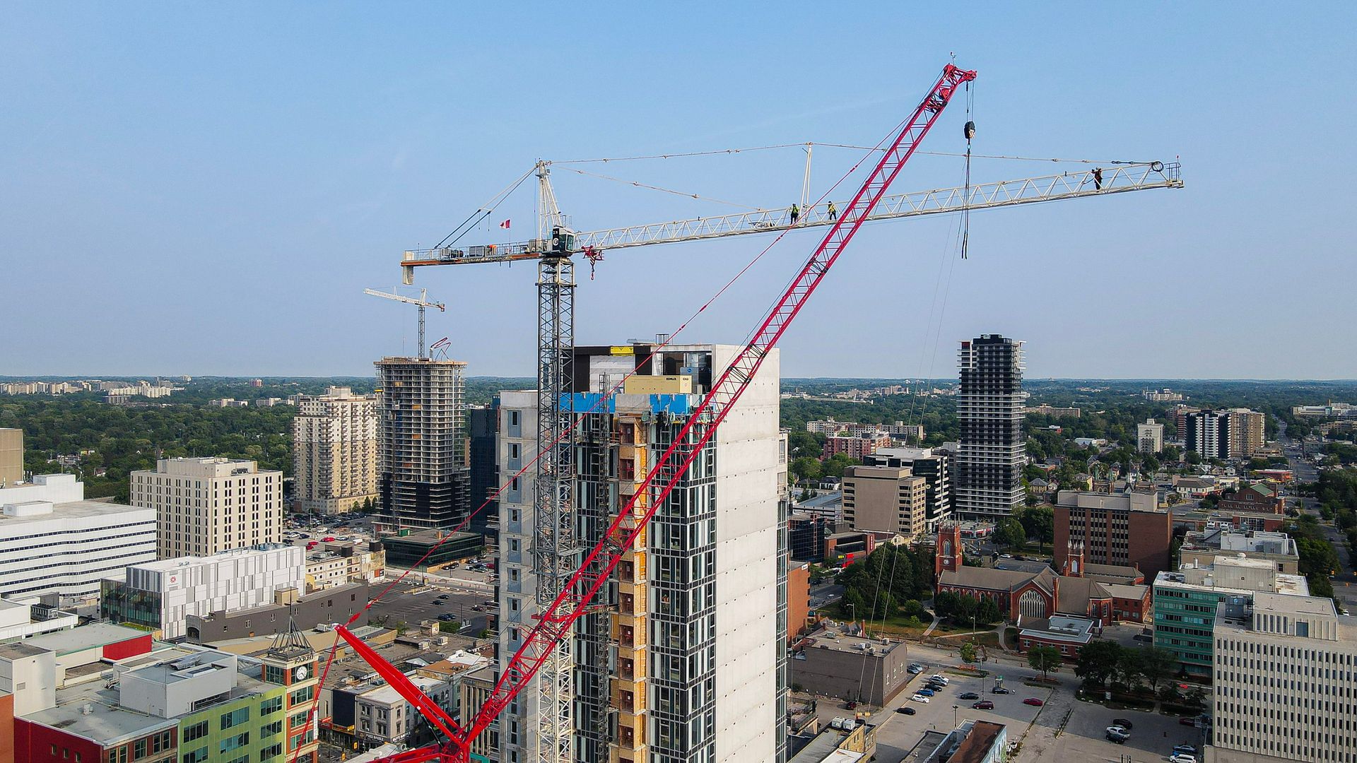 Construction site with two cranes atop a tall building, cityscape in background under blue sky.