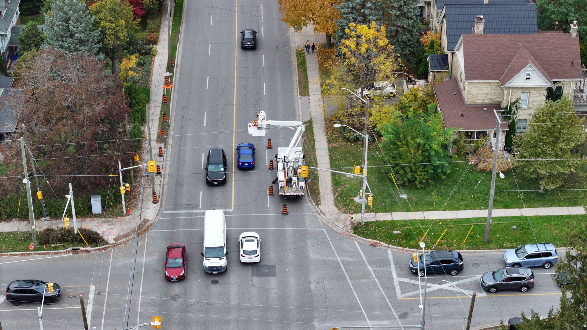 Overhead view of street with cars, a utility vehicle, and workers; autumn trees in the background.