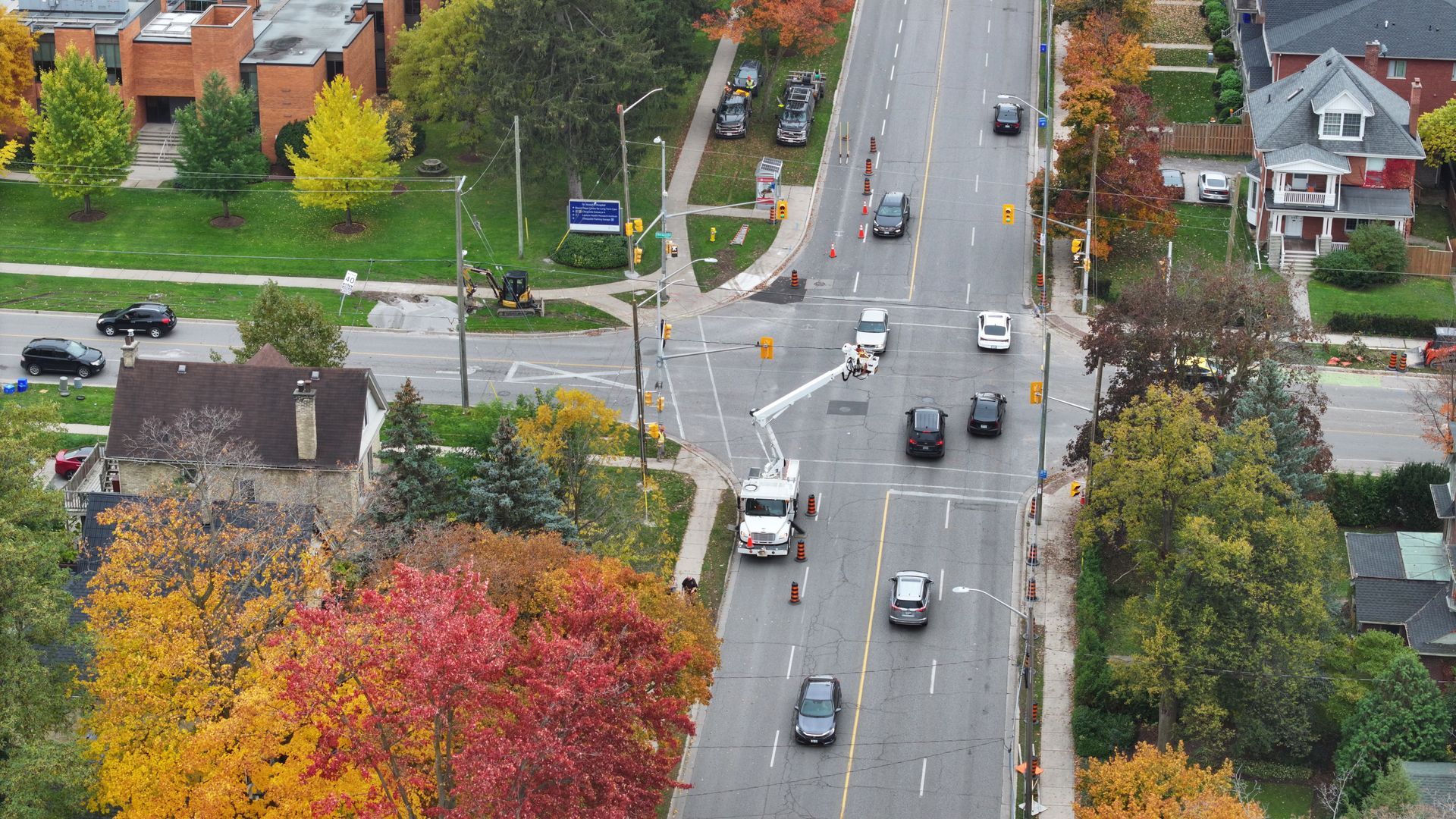 An aerial view of a road with cars driving by, fall foliage surrounds. A utility truck is also in the street.