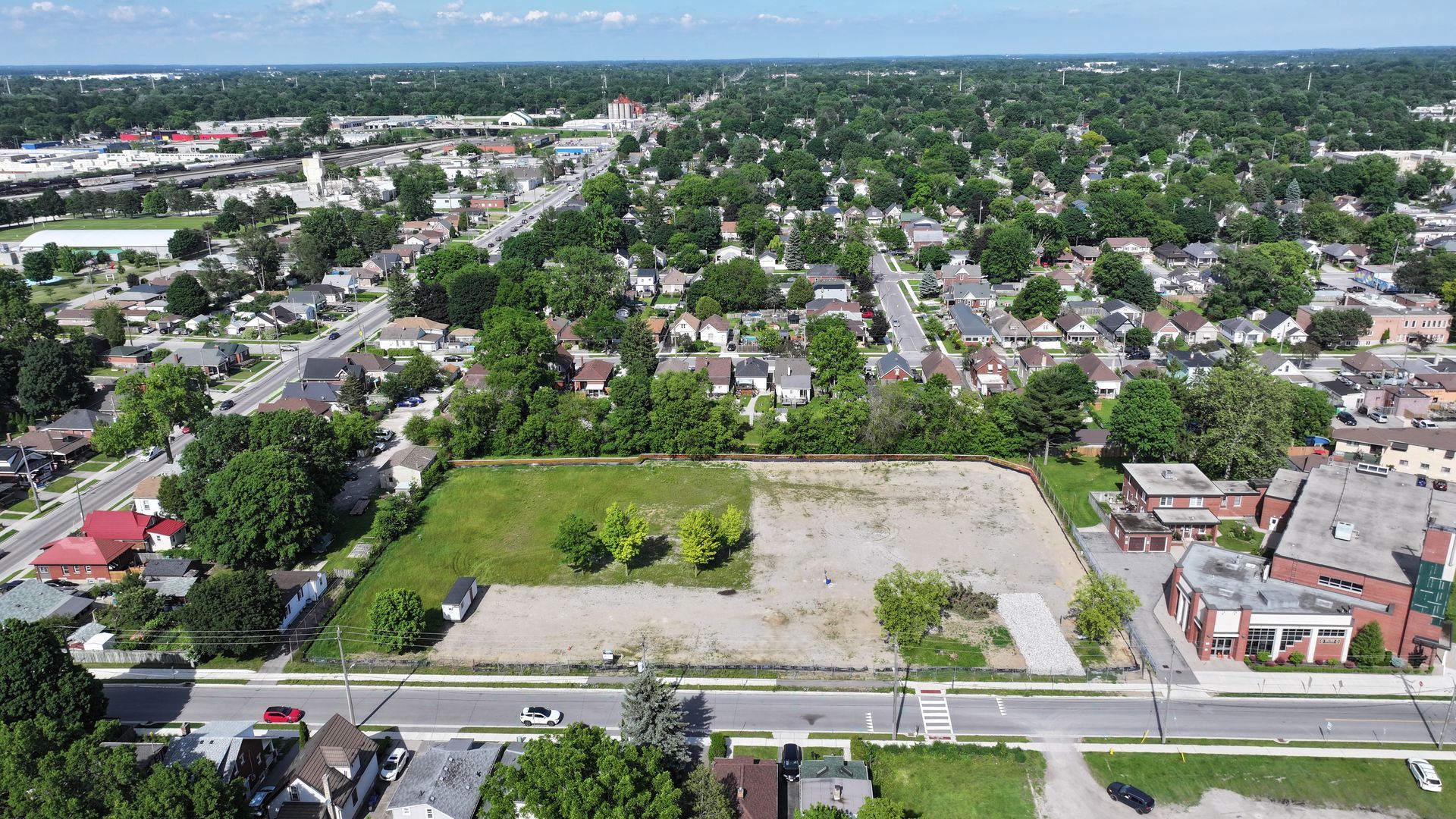 Aerial view of cleared lots and residential neighborhood on a sunny day. Trees and buildings fill the background.