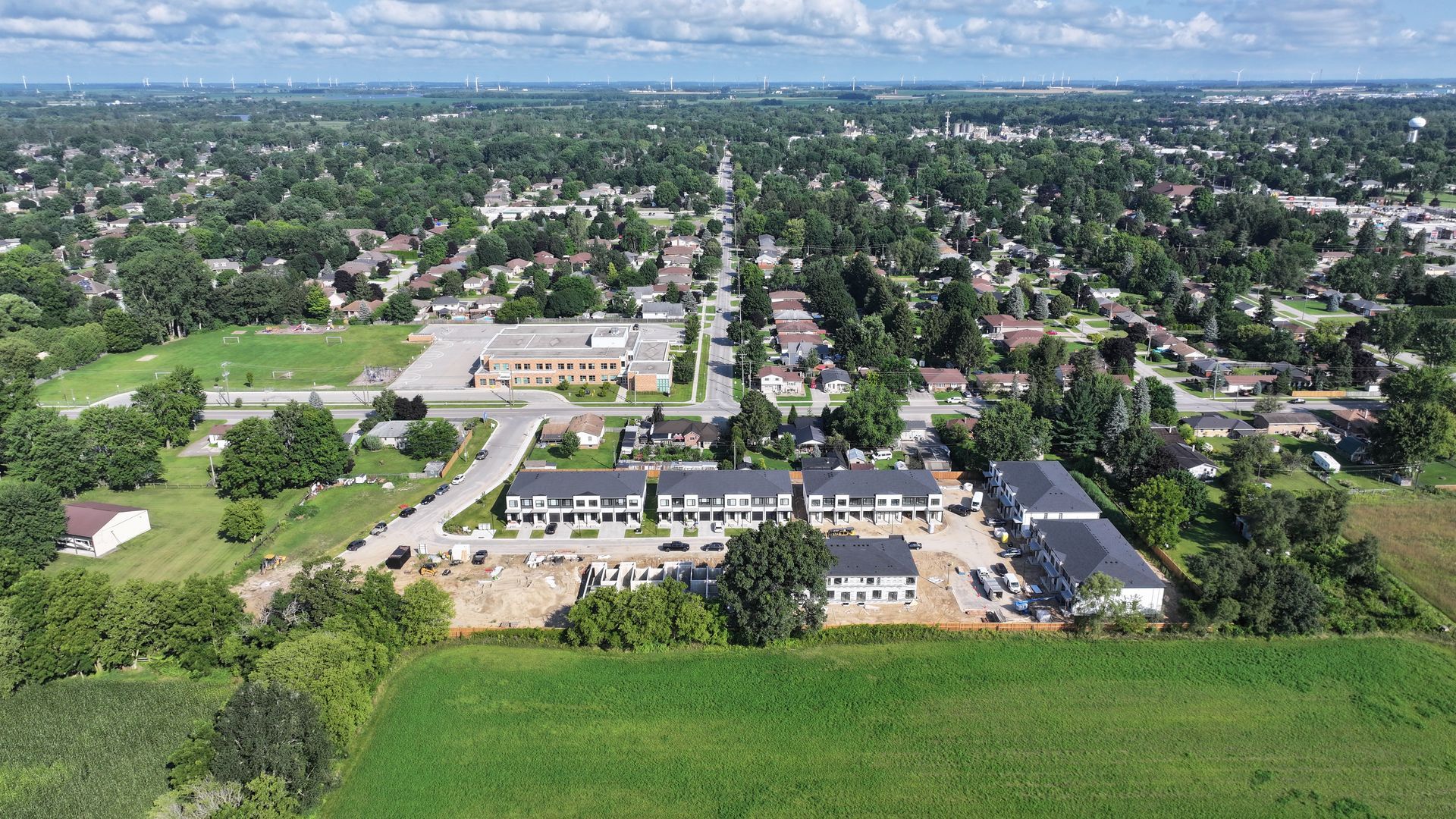 Aerial view of a suburban neighborhood with houses, a school, and green fields under a sunny sky.