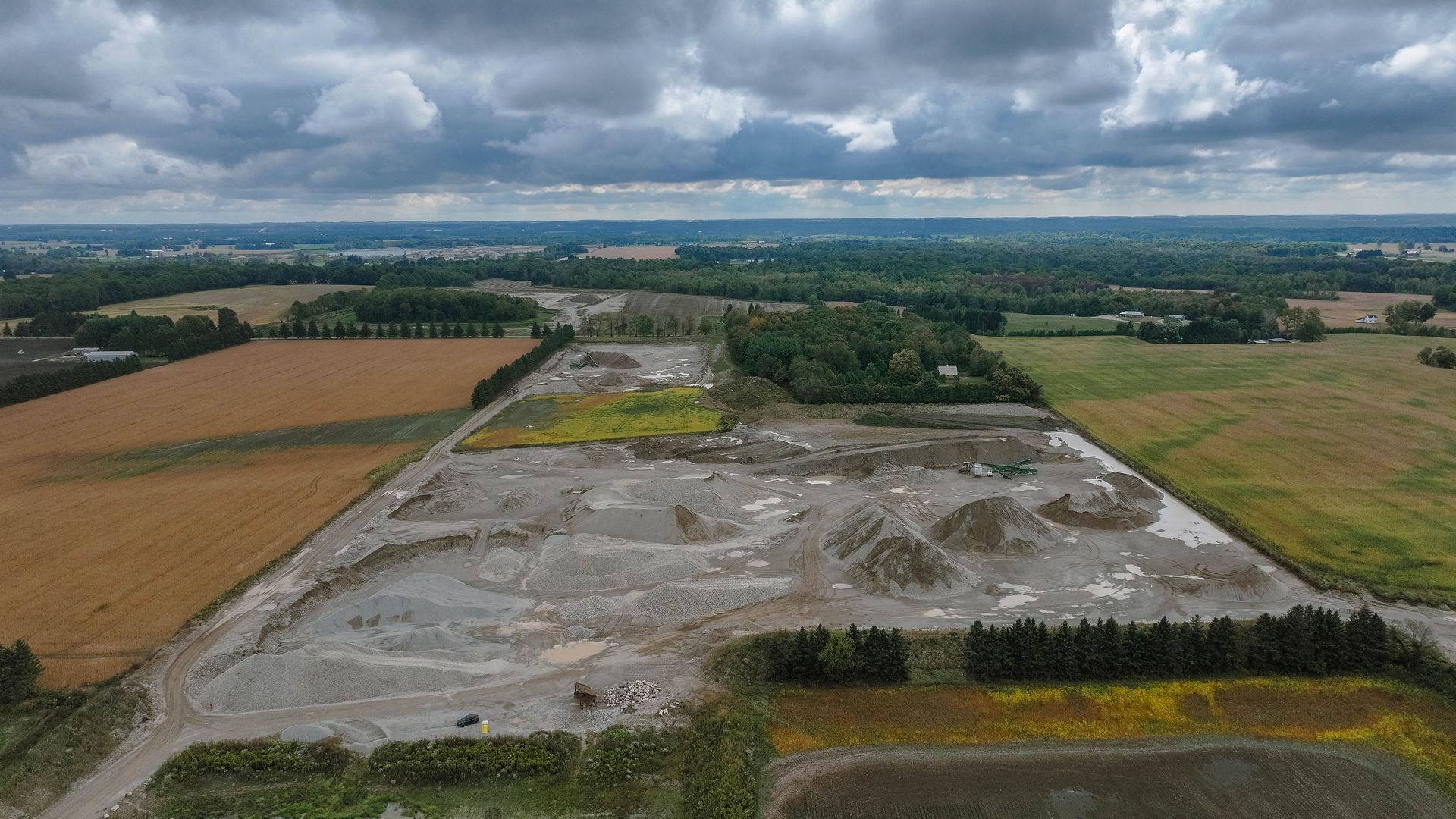Aerial view of a gravel pit surrounded by agricultural fields under a cloudy sky.