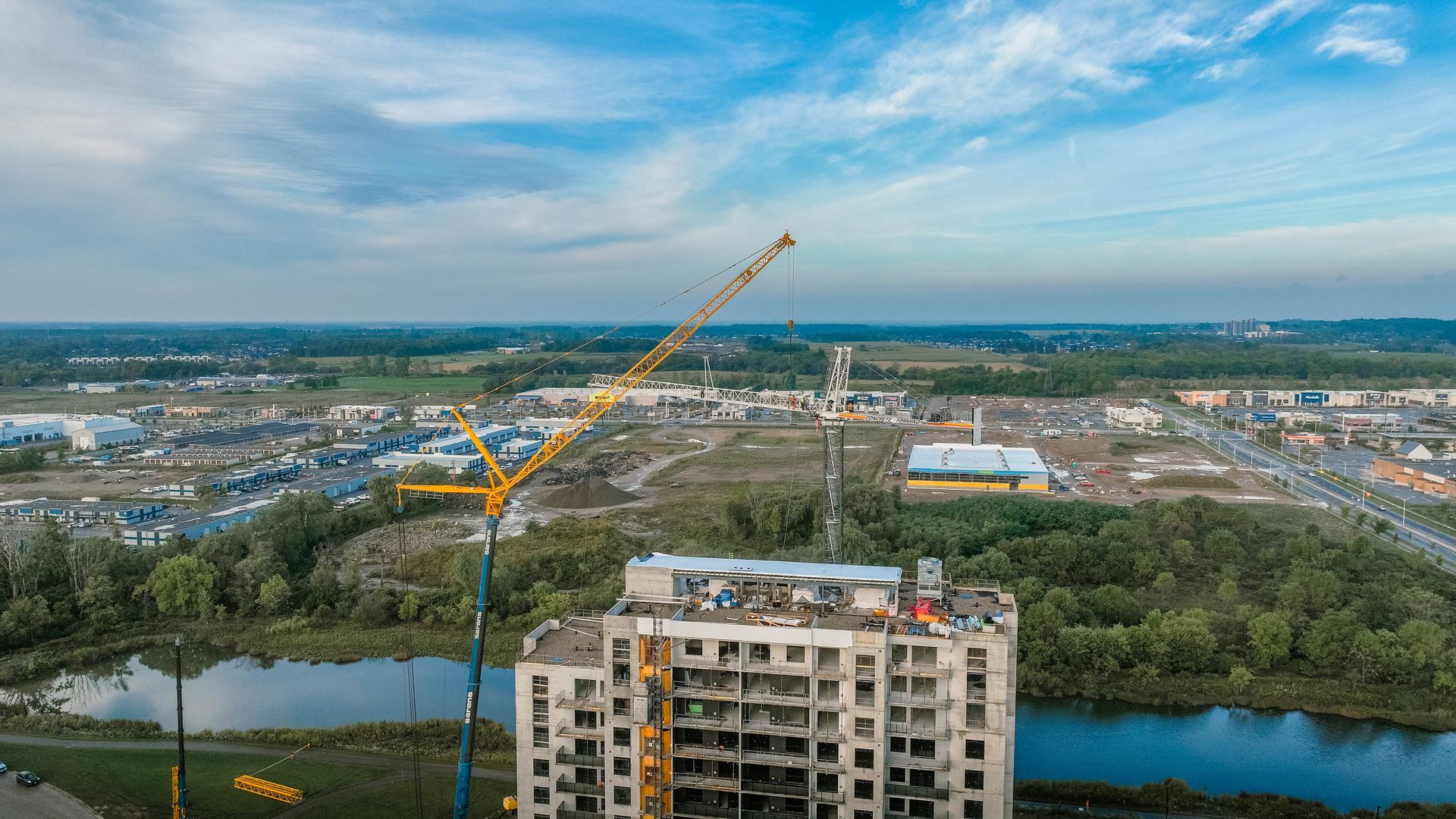 Construction crane atop a partially built, multi-story building overlooking a town and body of water.