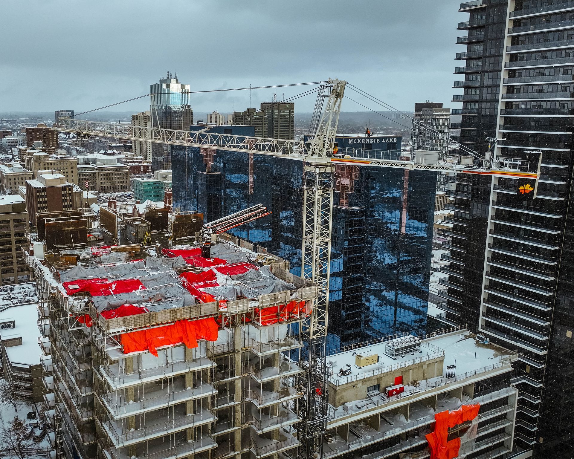 Construction site with crane, partially built skyscraper, and surrounding city buildings, under a cloudy sky.