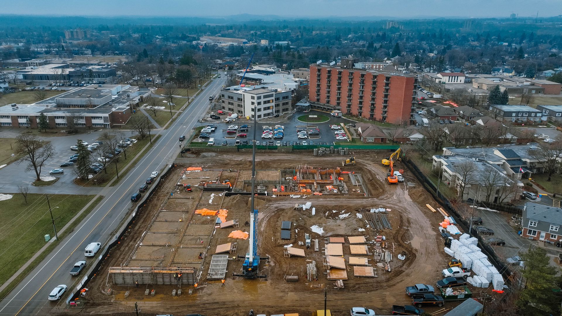 Aerial view of a construction site with a crane, surrounded by buildings and a road.