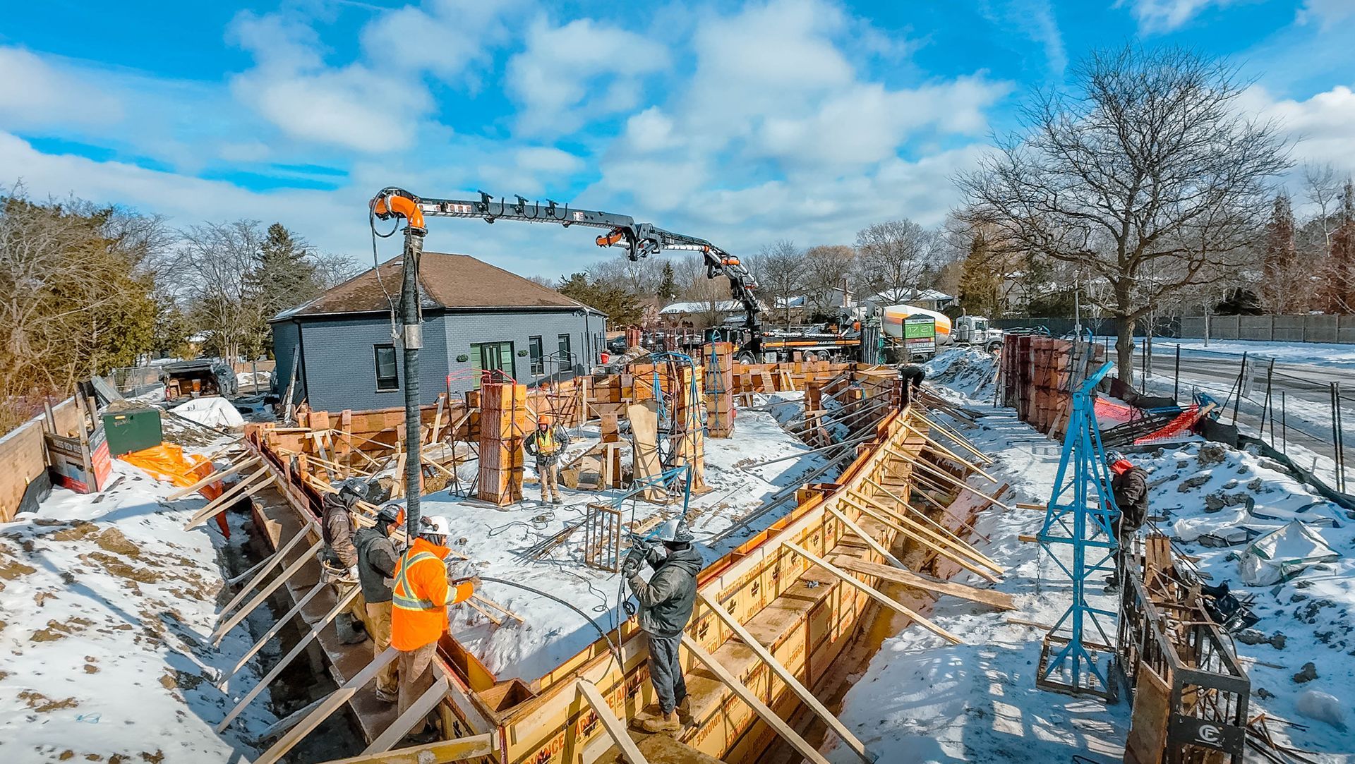 Construction site with workers pouring concrete into wooden forms in a snowy environment.