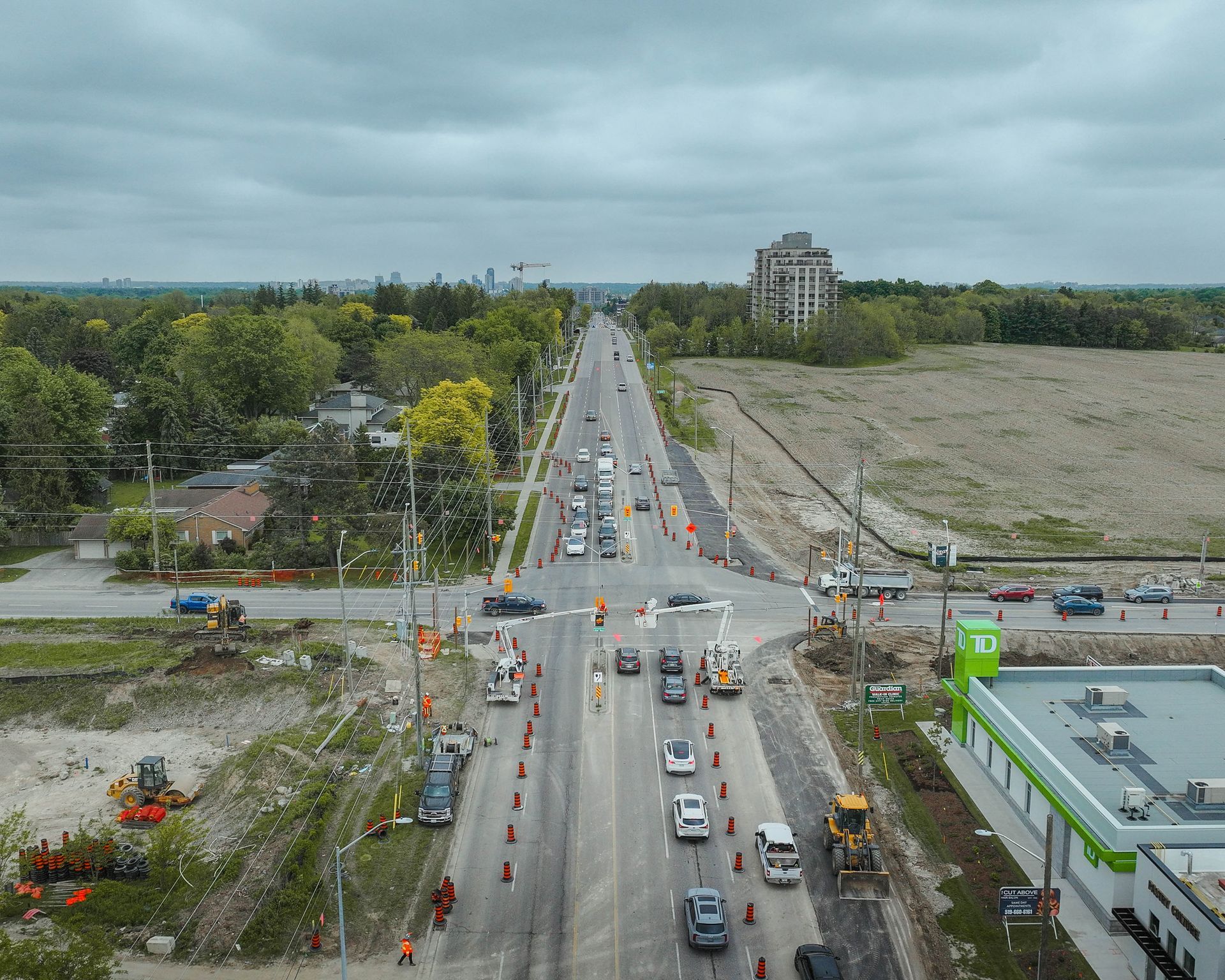 Aerial view of a road under construction with orange cones, cars, and construction equipment. Cloudy sky.