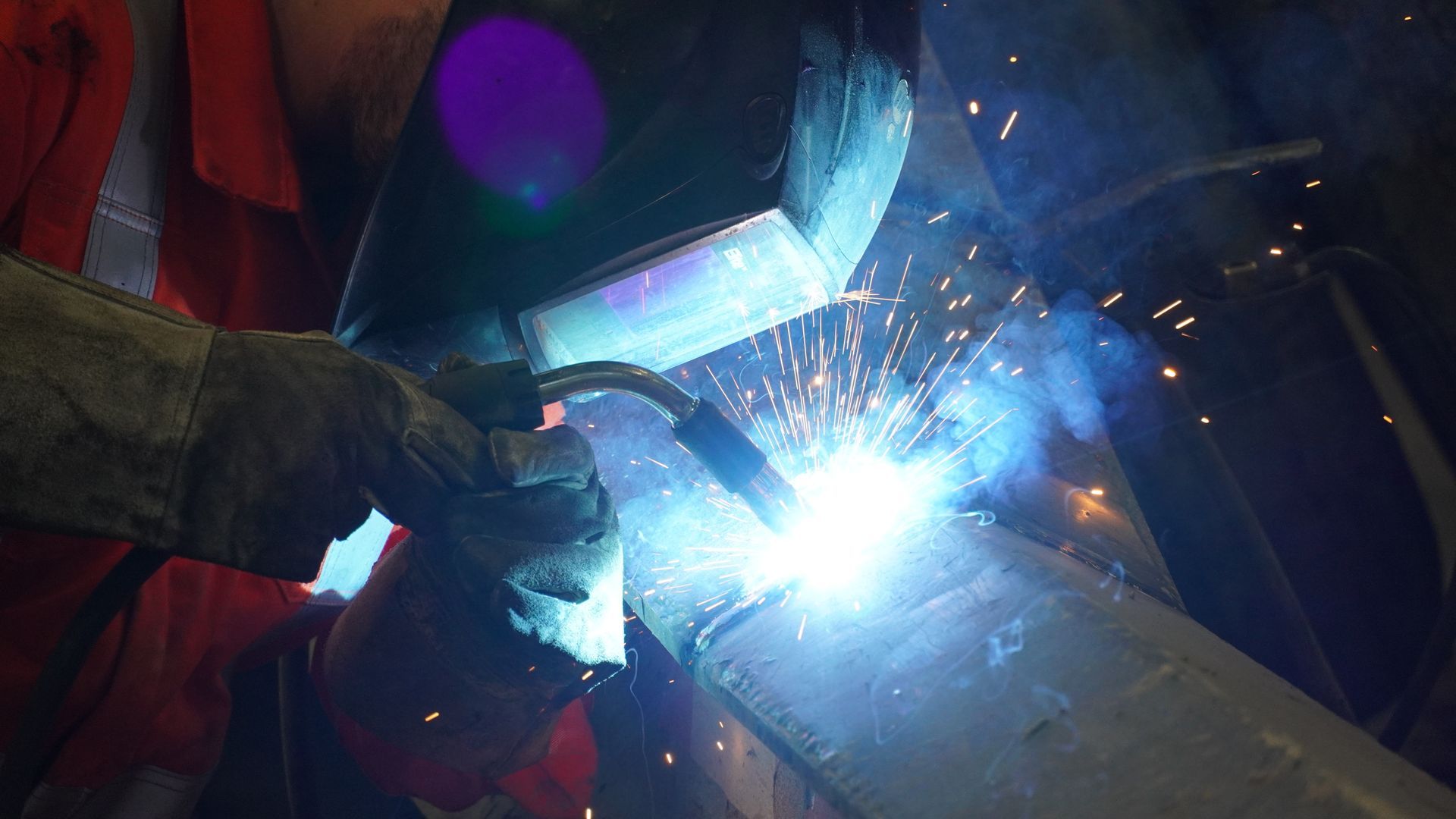 A man is welding a piece of metal in a factory.