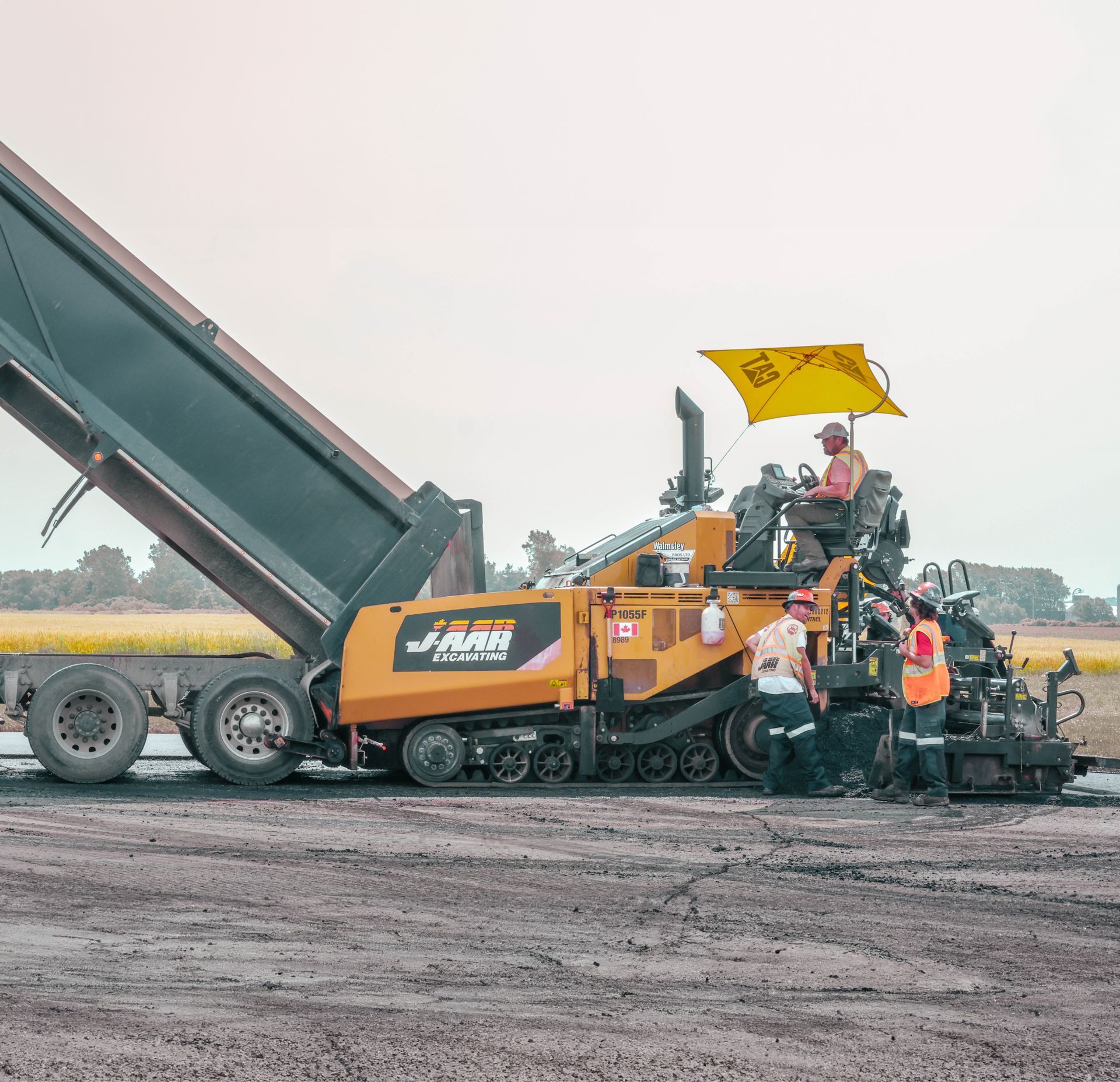 a yellow and black asphalt paver is being loaded onto a dump truck for paving services Ontario 