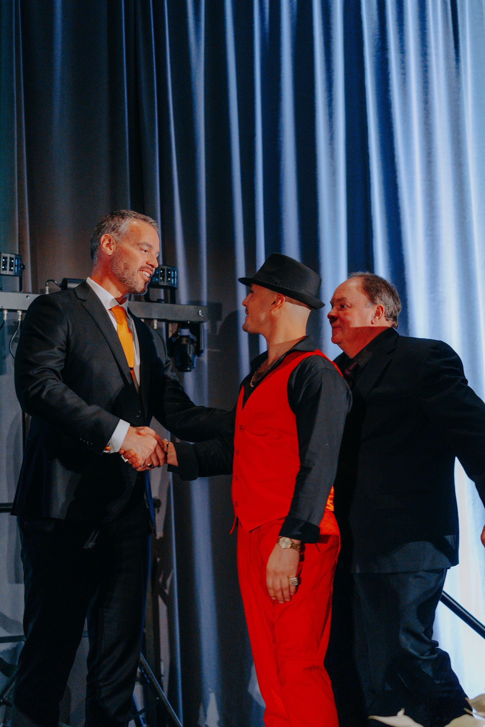 three men are shaking hands on a stage in front of a blue curtain .