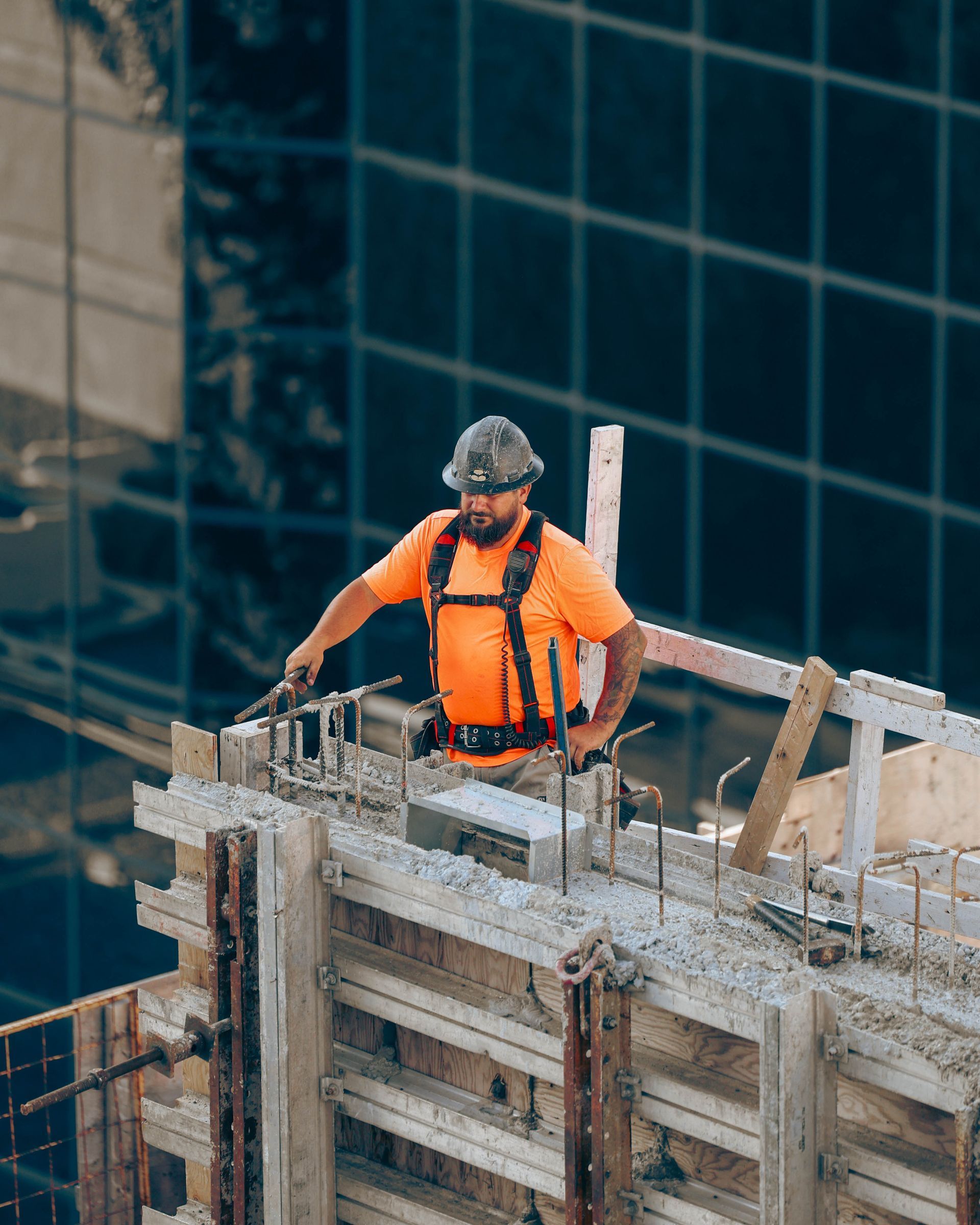 Construction worker in orange shirt and hard hat working on concrete formwork on a high-rise building site.