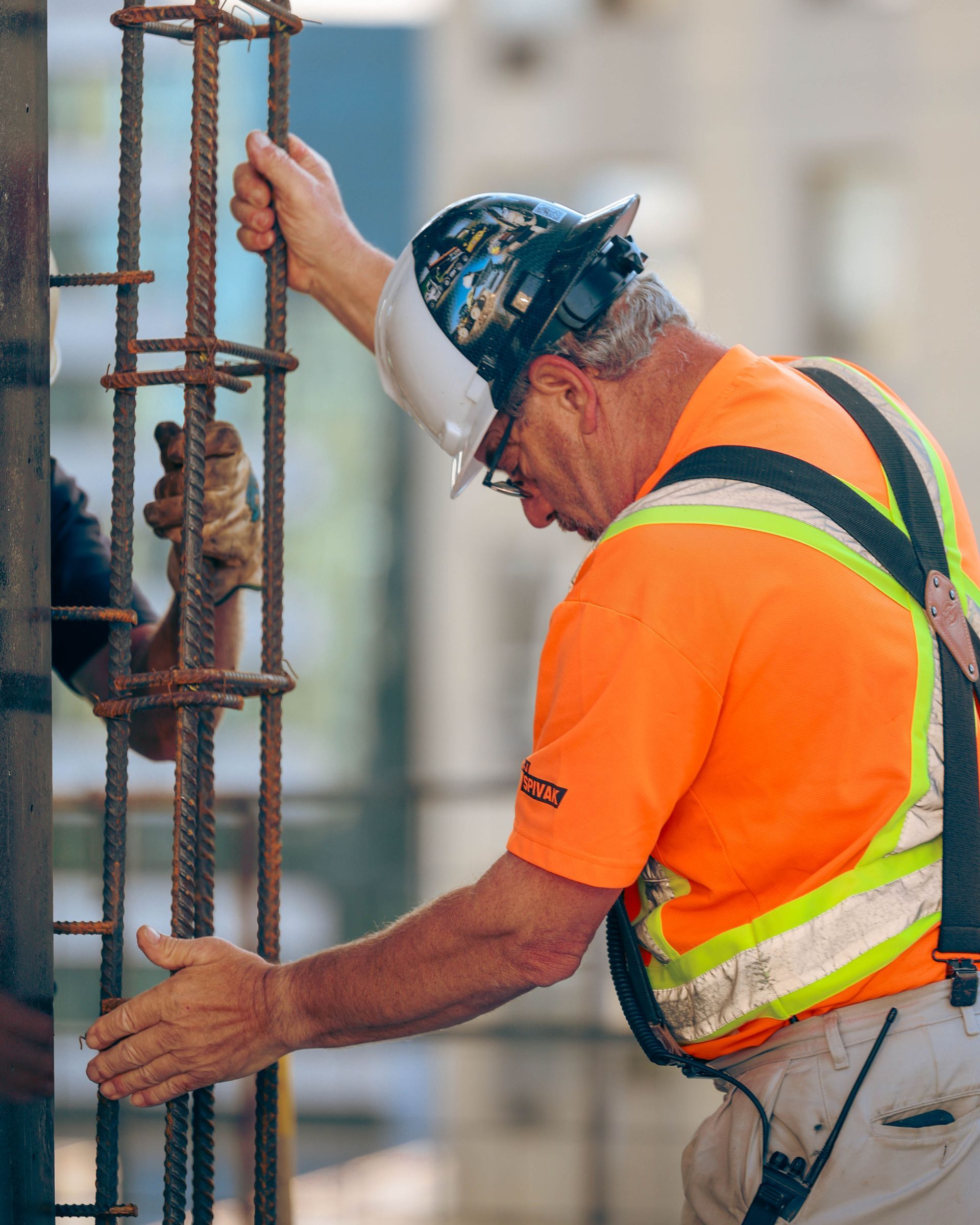 Construction worker wearing orange and a hard hat inspecting rebar.