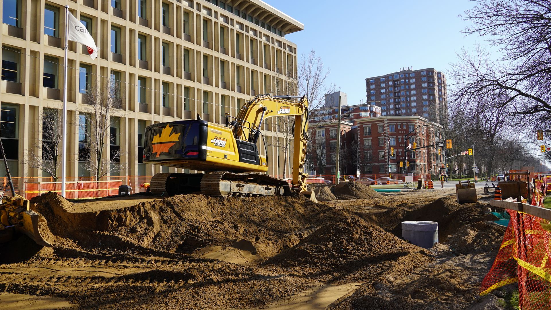 A large yellow excavator is digging a hole in the ground in front of a large building.