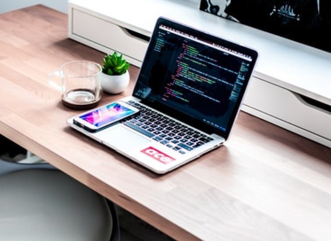 A laptop computer is sitting on a wooden desk next to a cell phone.