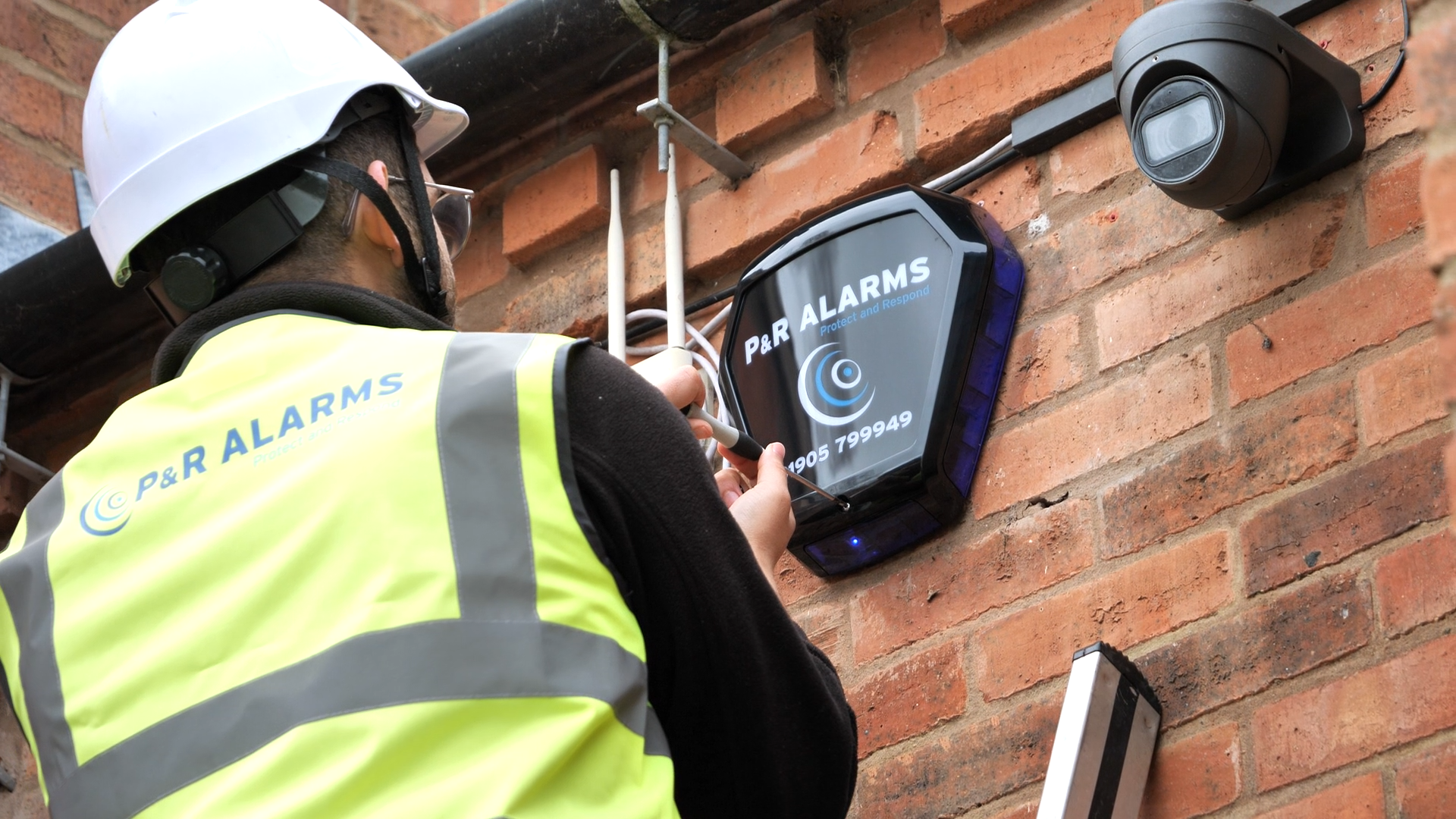 Construction worker in hard hat and safety vest installing a device on a wall.