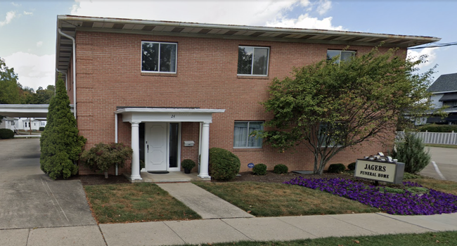 Two-story brick apartment building with white entryway, sidewalk, and purple flowers along the front.