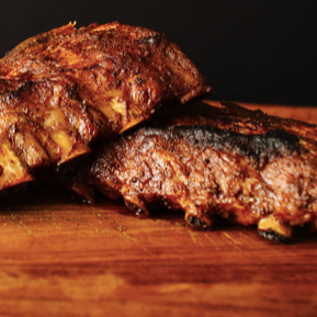 Two ribs are stacked on top of each other on a wooden cutting board.