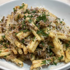 A close up of a plate of pasta with meat and cheese on a table.