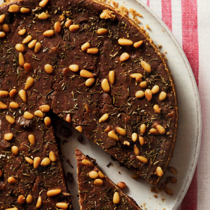 A chocolate cake with pine nuts on top has a slice taken out of it