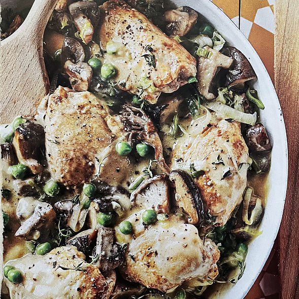 A white bowl filled with chicken , mushrooms and peas with a wooden spoon in it.