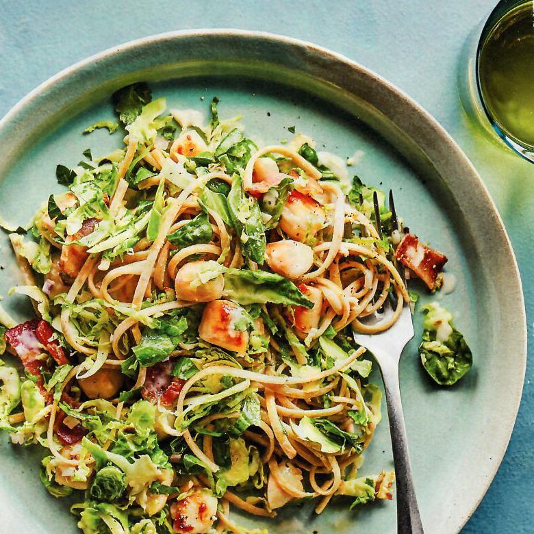A plate of noodles and vegetables with a fork on a table.