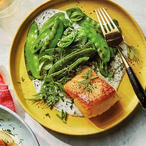 A yellow plate topped with a piece of fish and green beans with a fork.