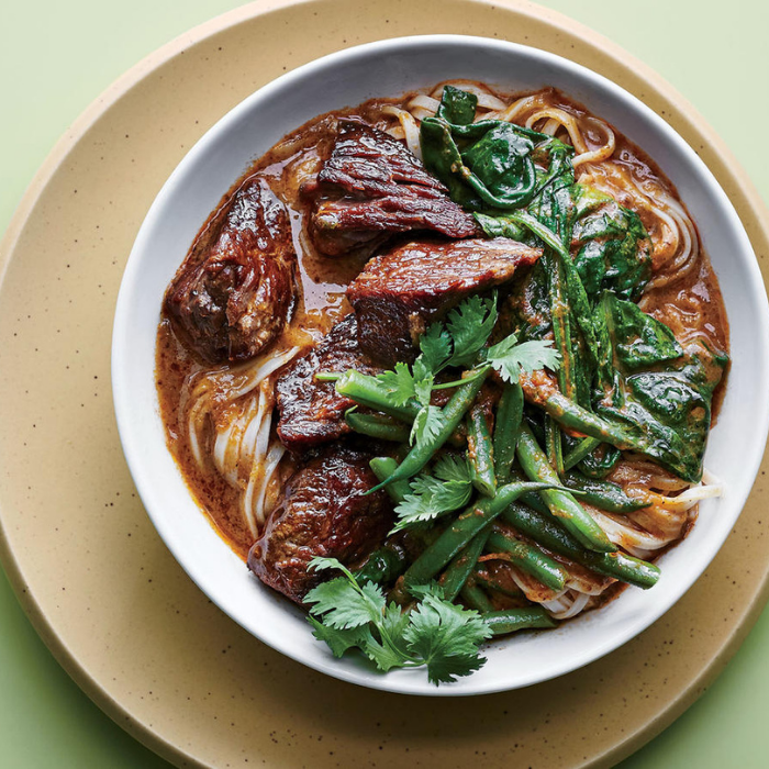 A bowl of beef noodles and green beans on a plate