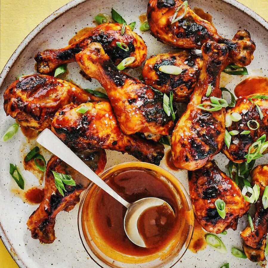 A plate of grilled chicken with a bowl of sauce and a spoon.