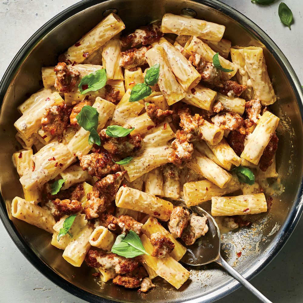 A pan filled with pasta and meat with a spoon in it.
