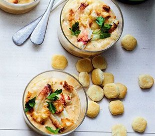 Two bowls of soup with crackers and spoons on a table.