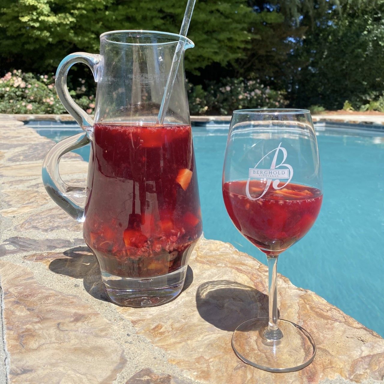 A pitcher and a glass of red liquid next to a pool