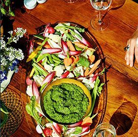 A wooden table topped with a plate of vegetables and a bowl of green sauce.