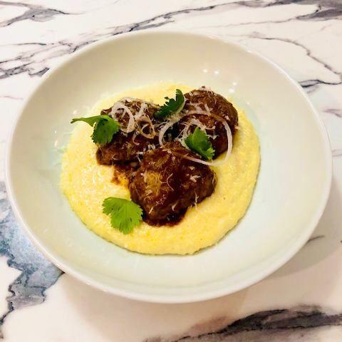 A white bowl filled with polenta and meatballs on a table