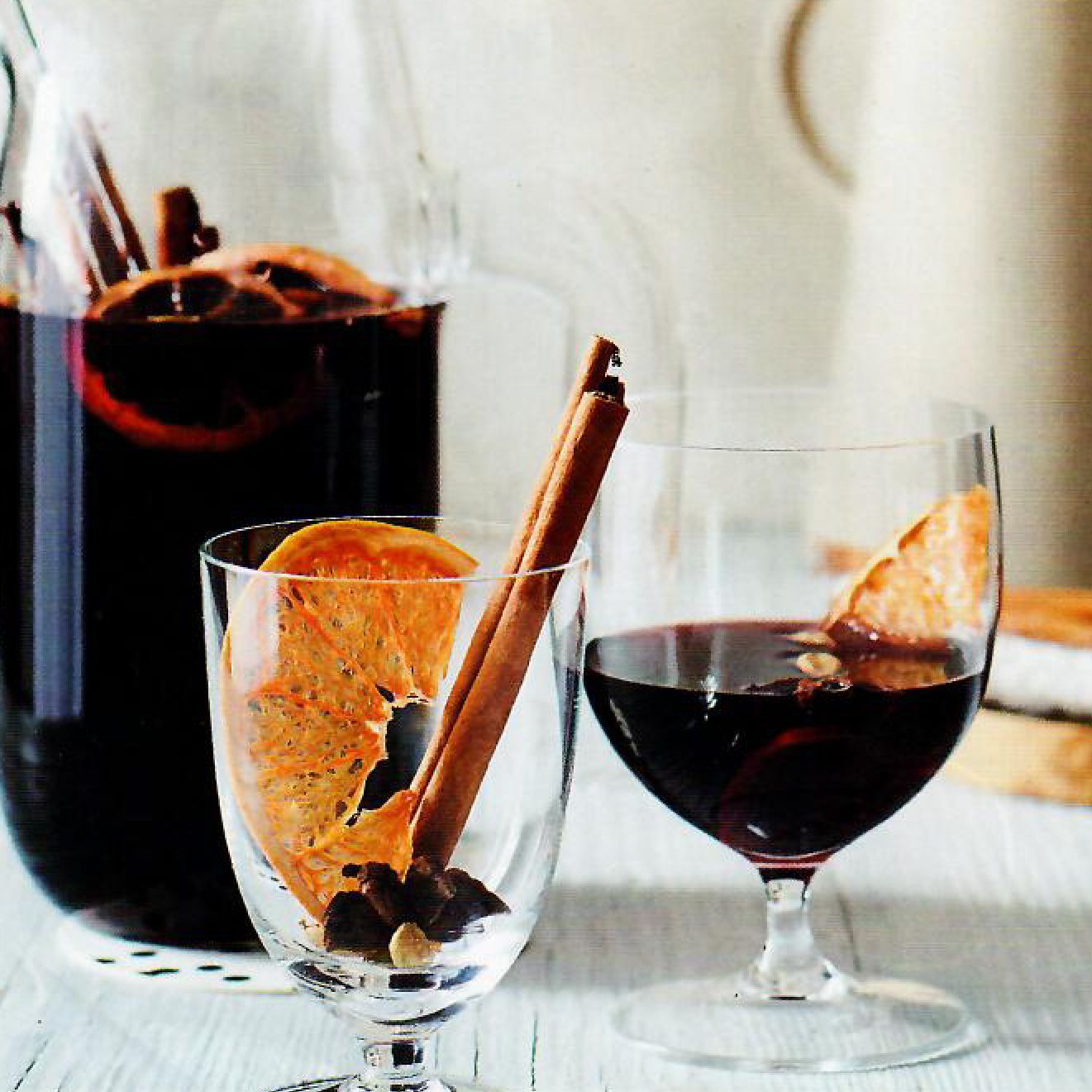 A glass of wine with cinnamon sticks in it next to a pitcher of wine