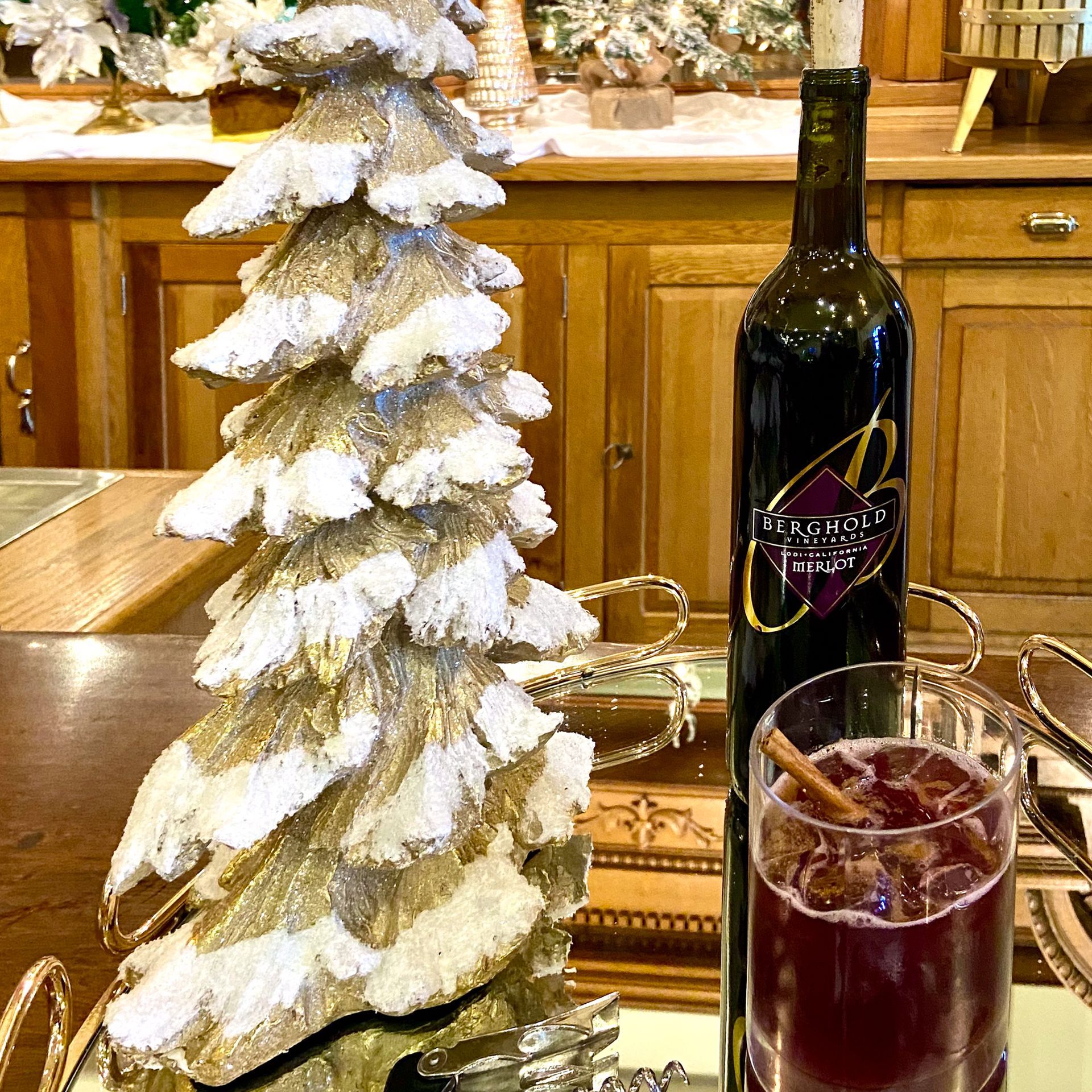 A bottle of wine and a glass of wine are on a table next to a christmas tree.