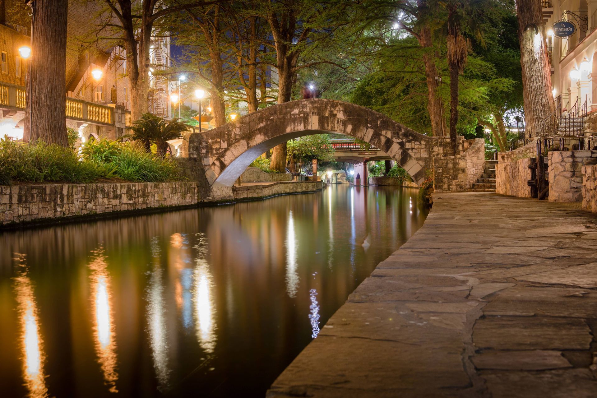 San Antonio River Walk at night with stone bridge and canal reflections