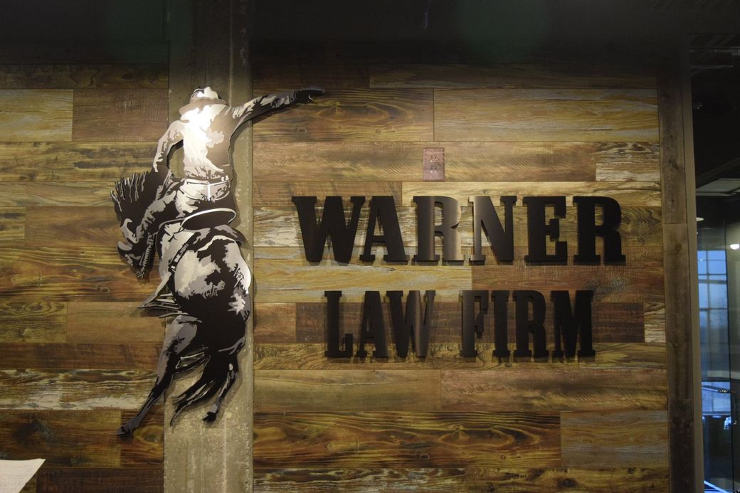 Warner Law Firm sign on a wood-paneled wall with a black figure graphic