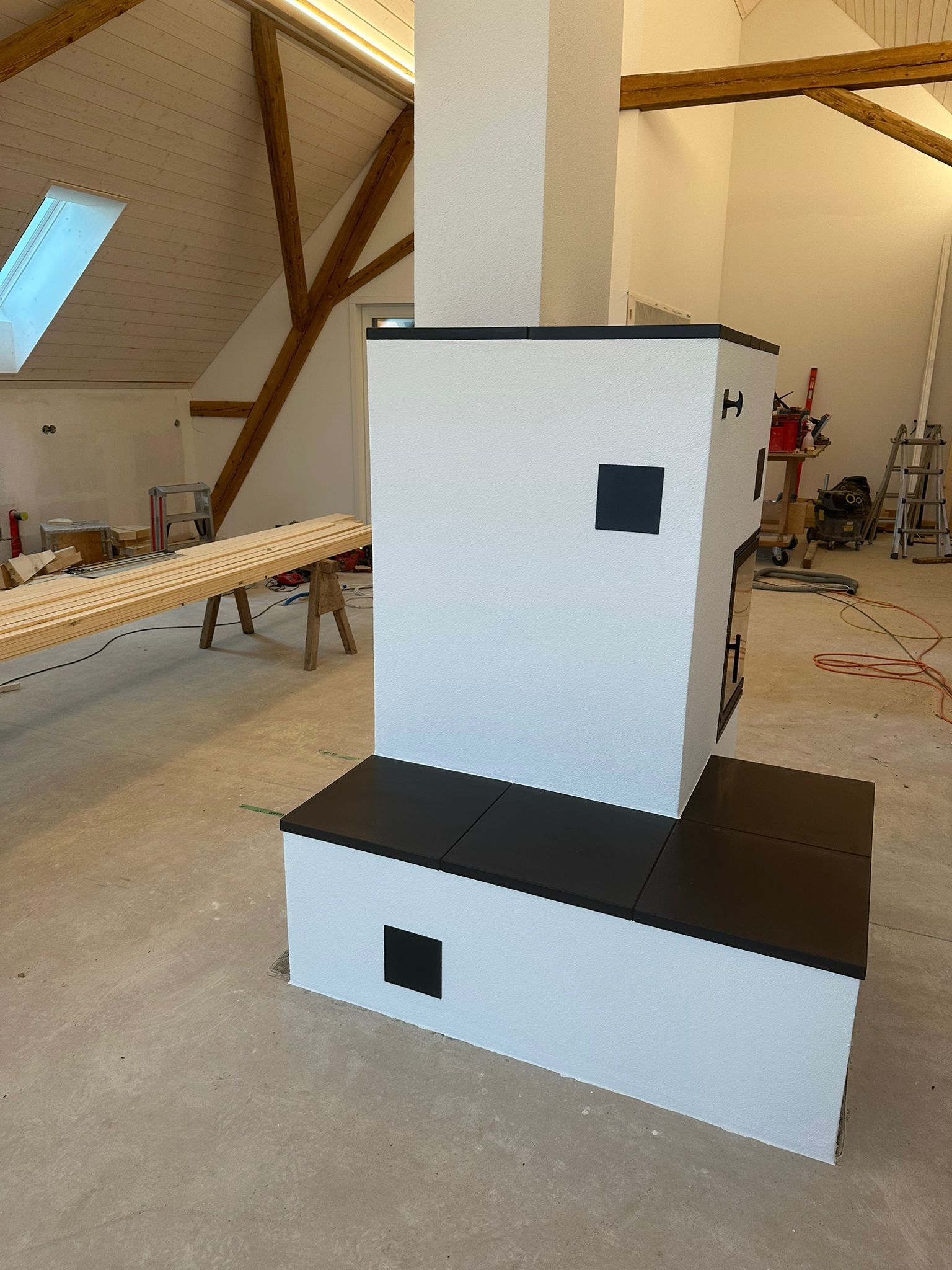 Ein weiß-schwarzer Backsteinofen in einem Raum mit freiliegenden Holzbalken.