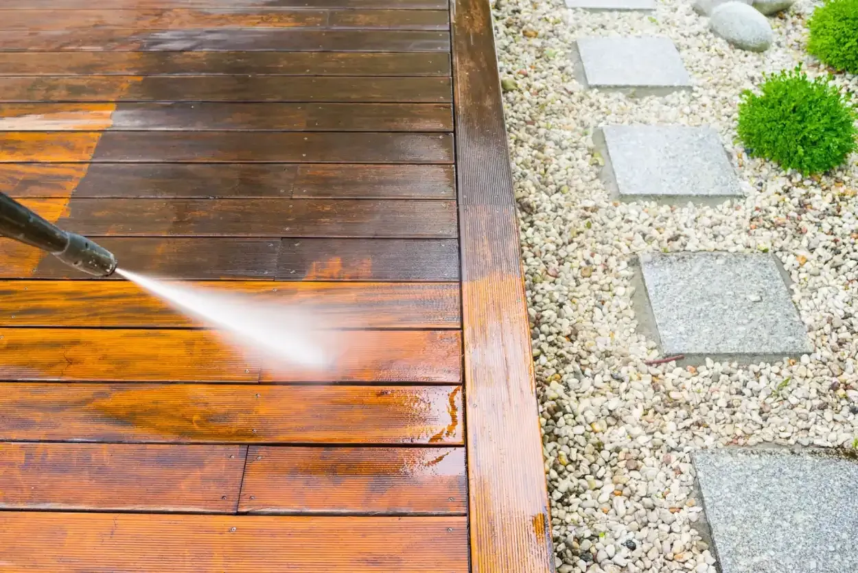 Pressure washing a wet wooden deck beside a gravel path and stepping stones