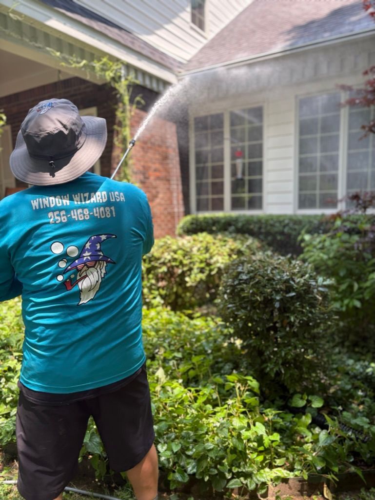 Worker in teal shirt pressure-washes a house exterior beside a window. Pressure Washing & Window Cleaning in Huntsville