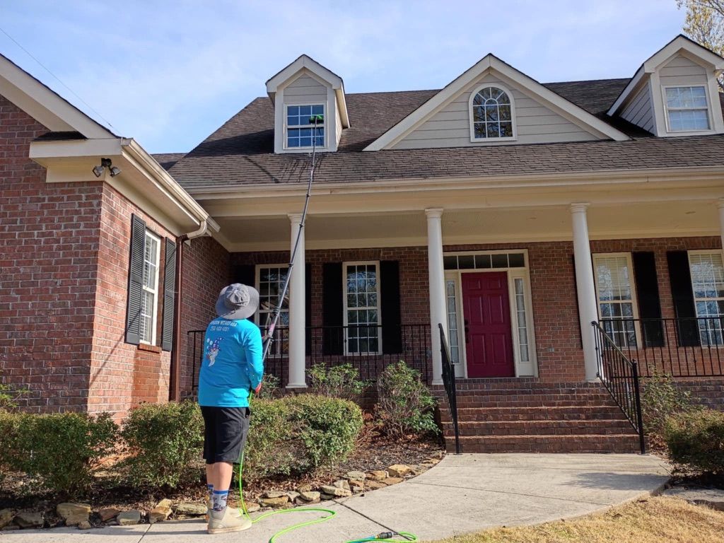 Person in blue jacket walking toward a brick house with a covered porch and red front door.