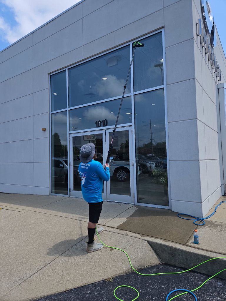 Person in blue jacket approaching a glass-front building entrance with a long pole.