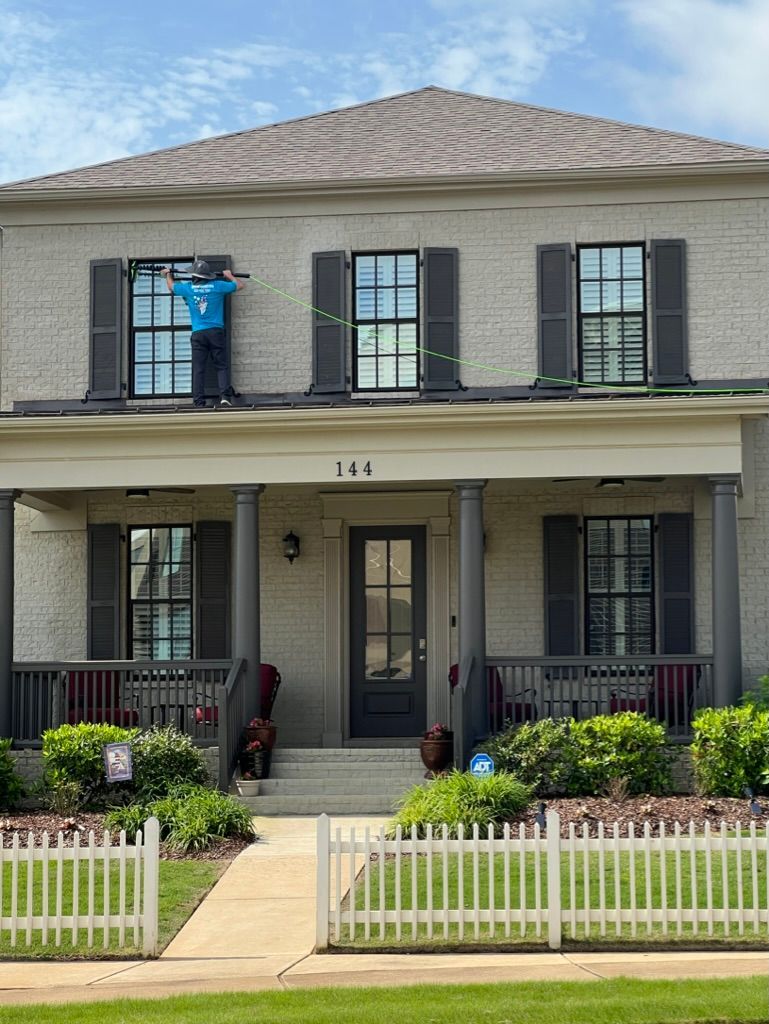 Two-story gray house with a front porch, white picket fence, and flower beds