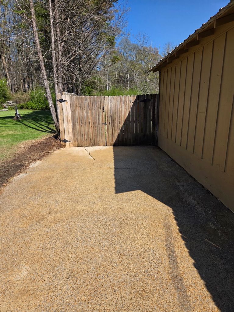 Gravel driveway beside a tan building, ending at a wooden fence in bright sunlight.
