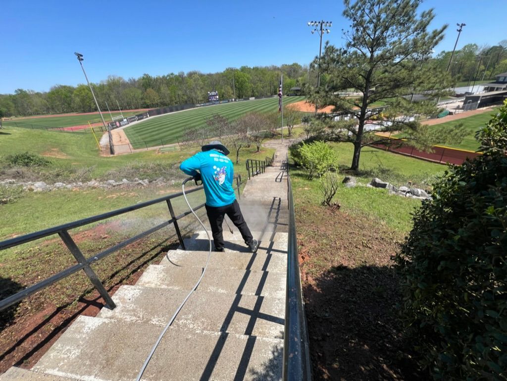 Person in a blue shirt walking down a concrete path with black railings in a sunny park.