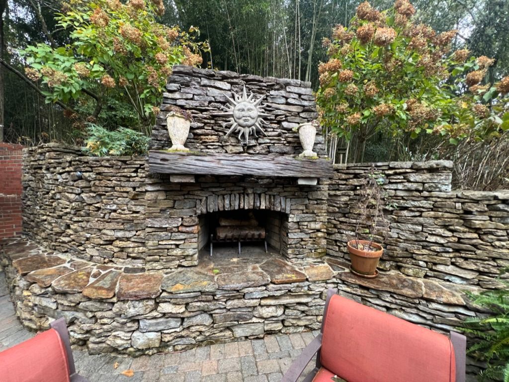 Stone outdoor fireplace with carved mantel, surrounded by a patio and greenery