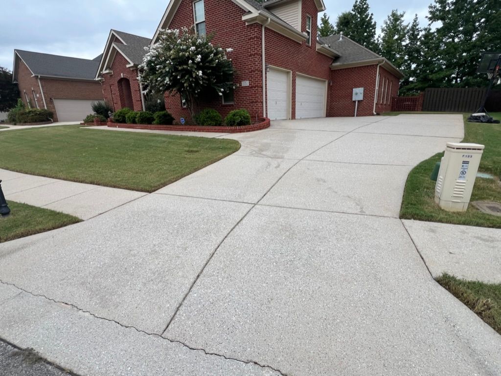 Suburban brick house with a wide concrete driveway and manicured lawn.