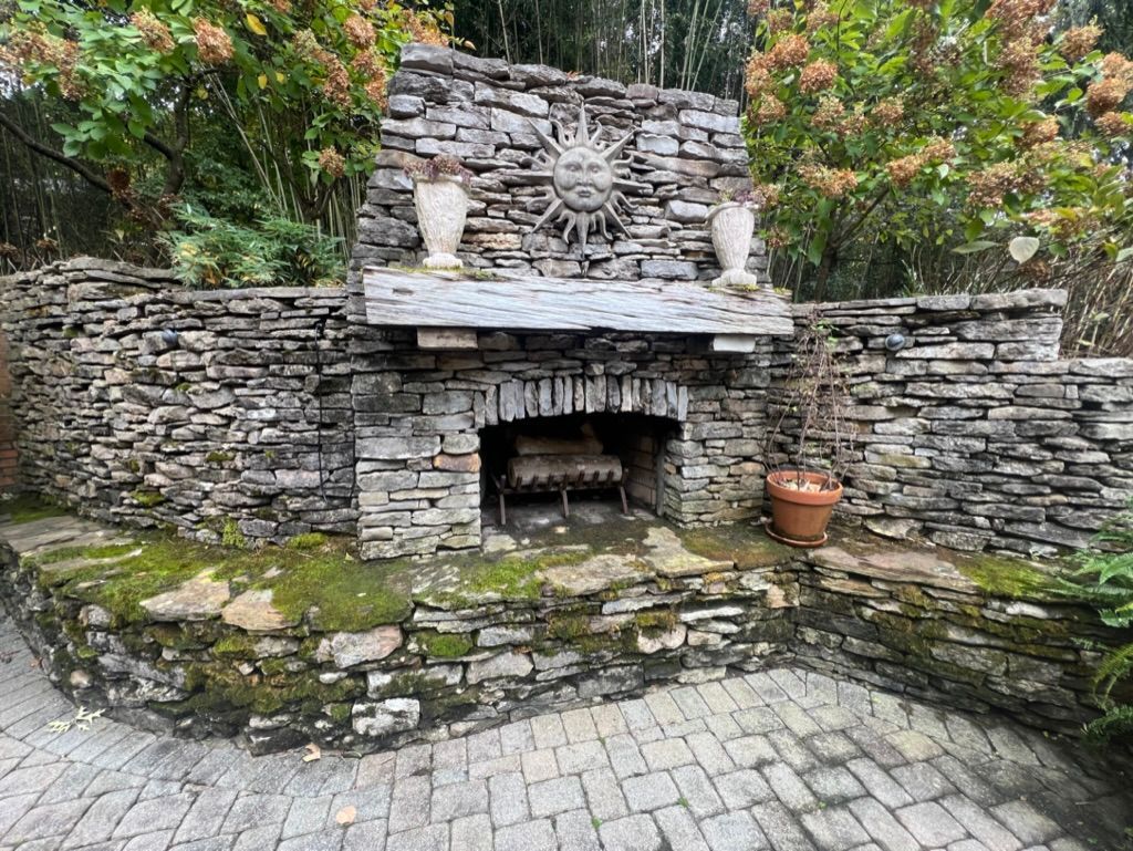 Stone outdoor fireplace in a garden patio with potted plants and mossy steps